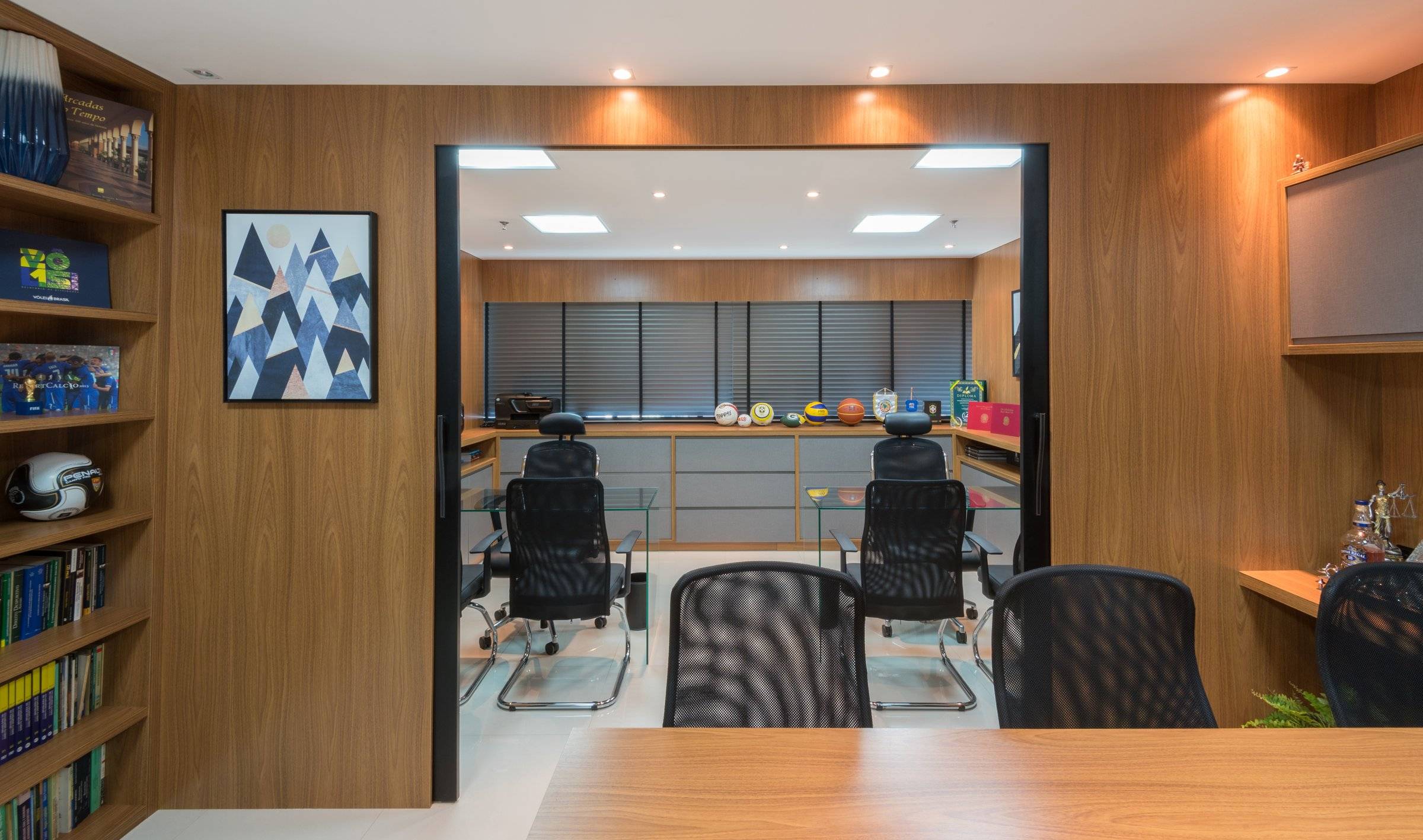 Sala com estante de livros e mesa de reuniões em madeira