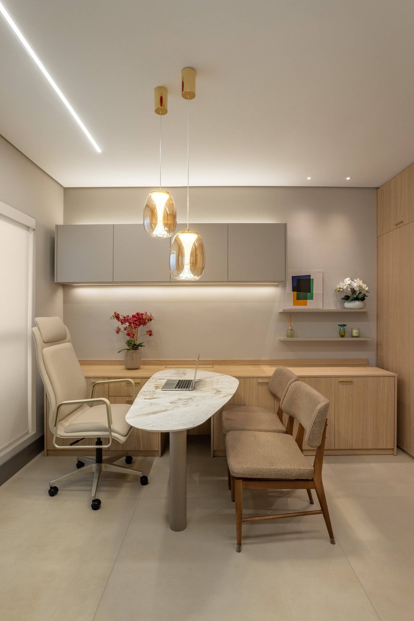 Consultório com mesa oval clara, cadeiras em madeira e pendentes âmbar sobre a mesa