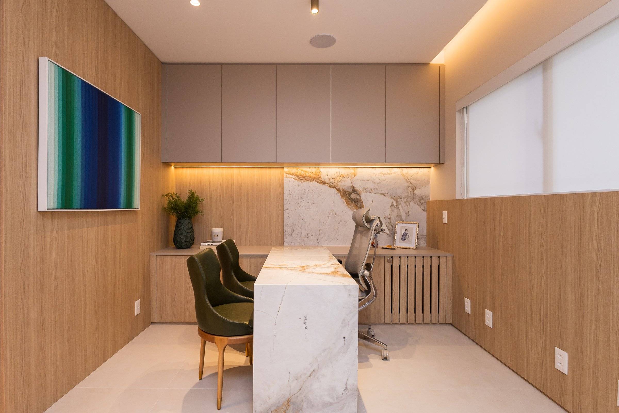 Consultório com mesa em mármore, poltronas verde-oliva e luz indireta