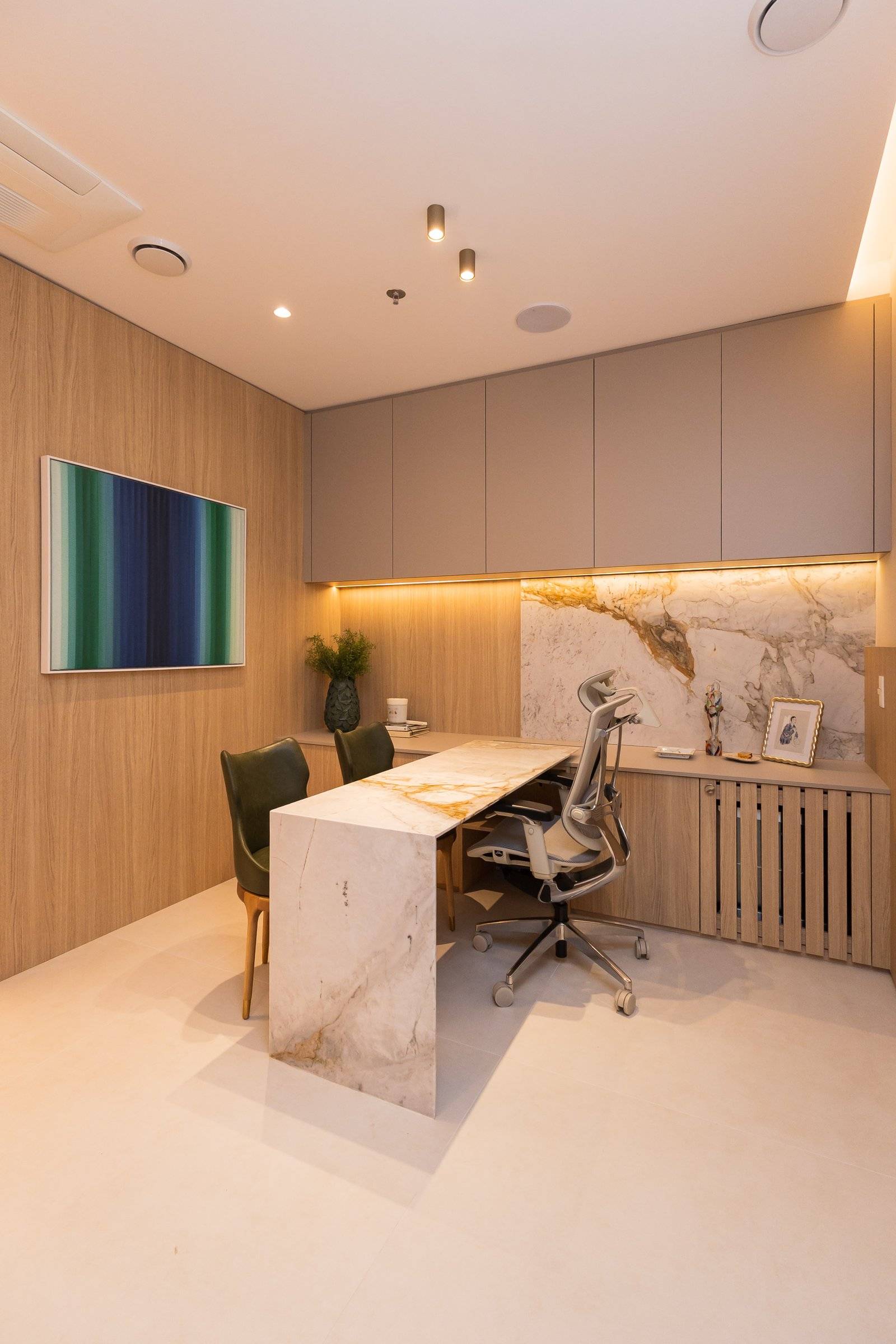 Consultório visto da porta, com mesa em mármore e quadro em tons de verde e azul
