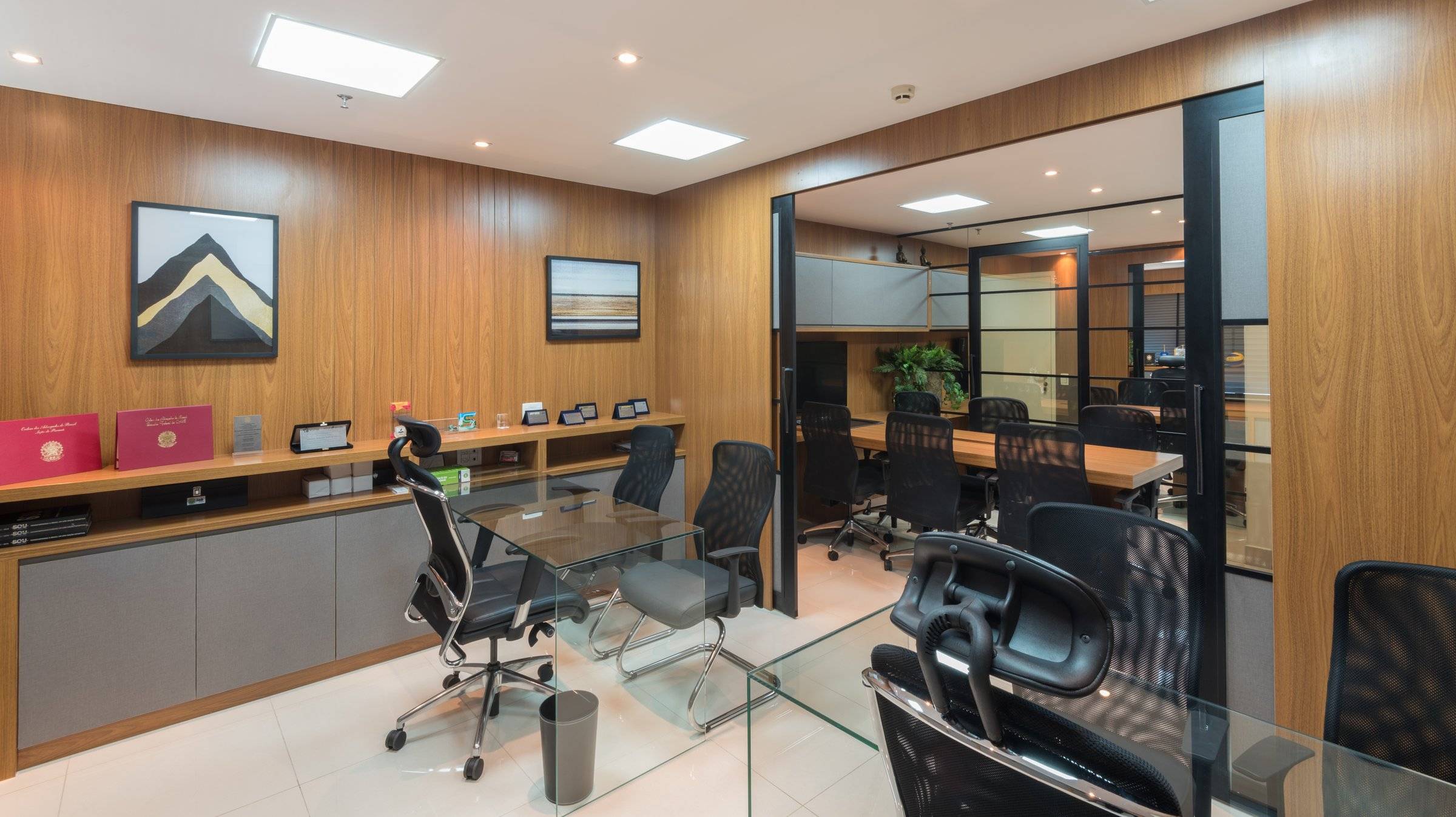 Sala de diretoria com mesa de vidro, cadeiras pretas e painéis de madeira