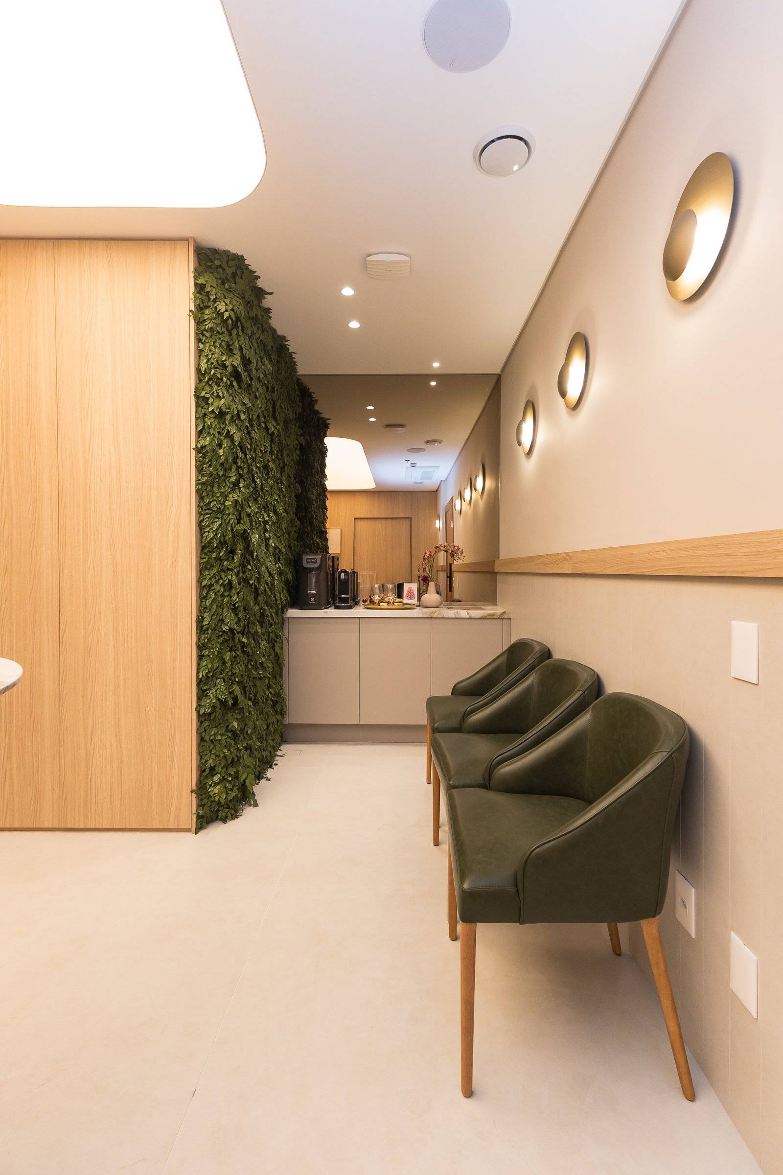 Sala de espera com jardim vertical e poltronas verde-oliva