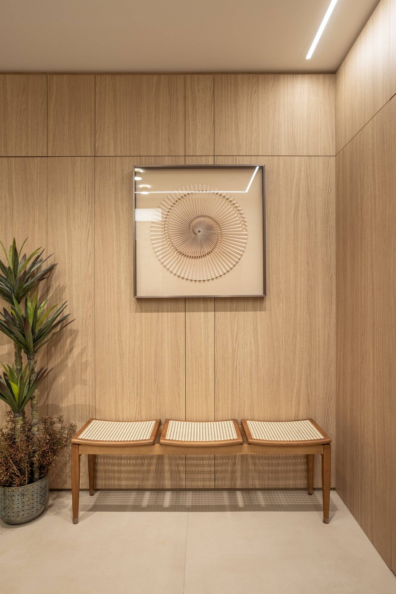 Banco de madeira e palha na espera, com quadro em relevo sobre painel de carvalho