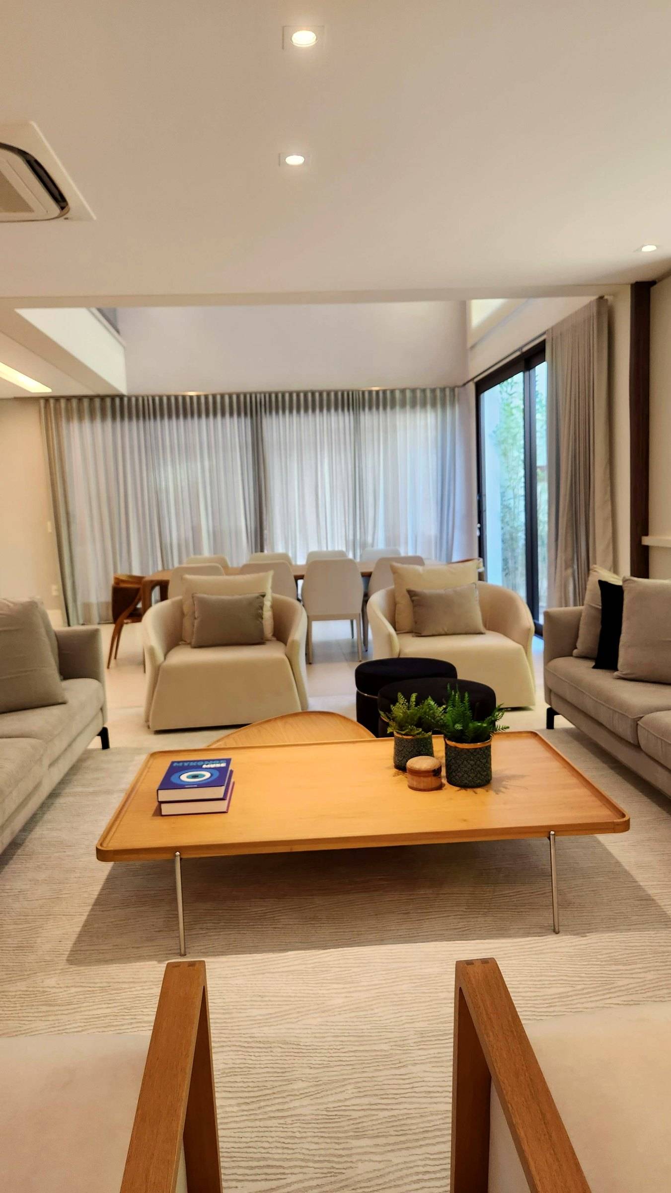 Poltronas claras e mesa de centro diante das janelas com cortinas