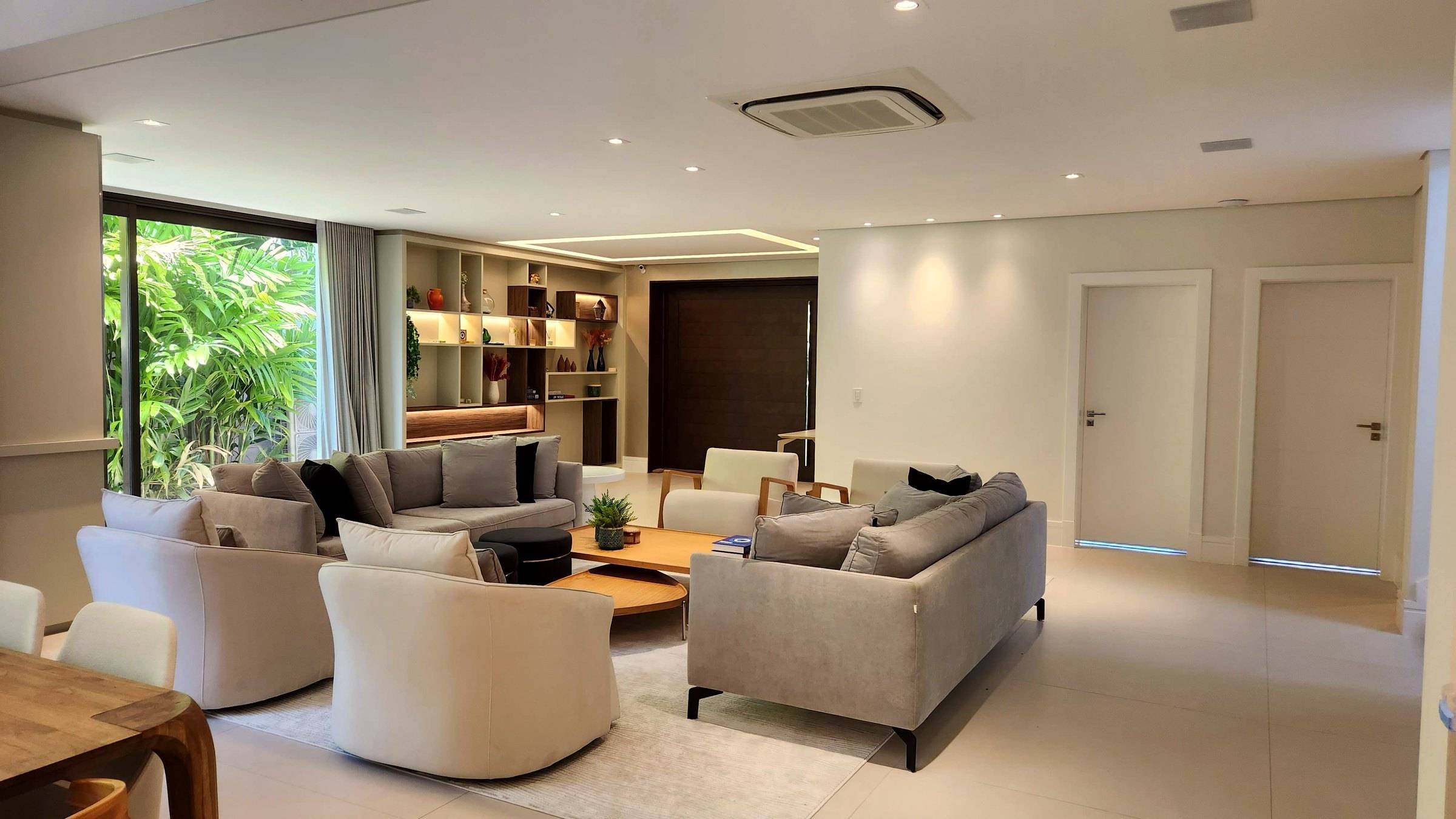 Living com poltronas claras e portas ao fundo