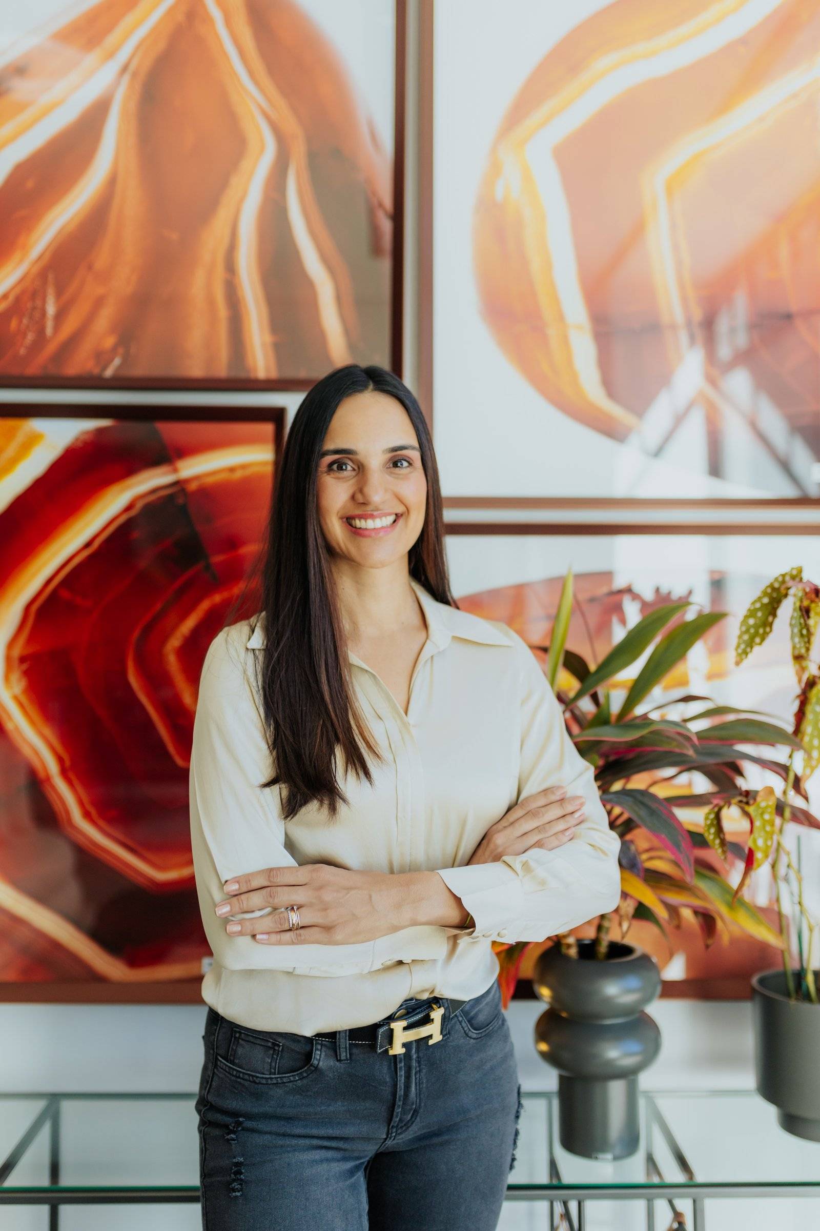 Isabella Porto de braços cruzados diante de quadros em tons de laranja